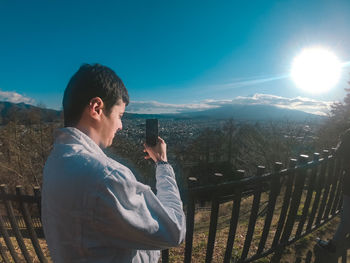 Man photographing while standing by railing against sky