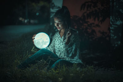 Young woman looking down while sitting on illuminated land