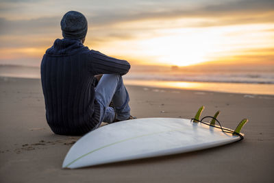 Man reading book on beach against sky during sunset