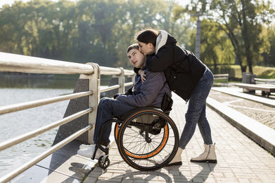 Girlfriend kissing boyfriend sitting in wheelchair at embankment