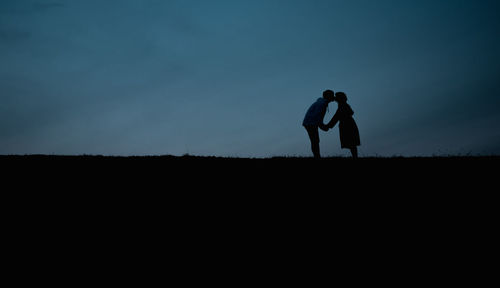 Silhouette couple kissing on landscape against sky during sunset