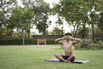 Young man sitting on grass against trees