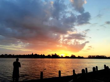 Silhouette people standing by sea against sky during sunset