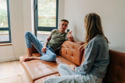 A young man is arguing with his girlfriend while sitting on the couch at home