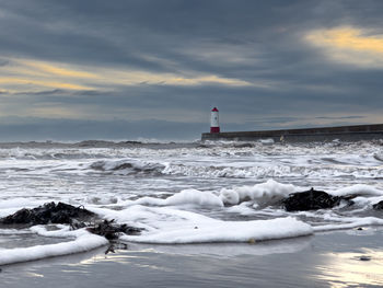 Lighthouse by sea against sky during sunset