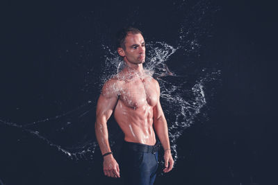 Shirtless man standing against black background