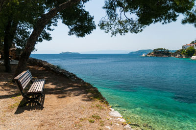 Empty bench on shore by sea against sky