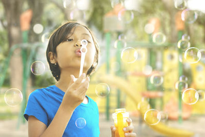 Girl blowing bubbles while standing in playground