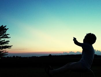 Silhouette boy sitting against sky during sunset