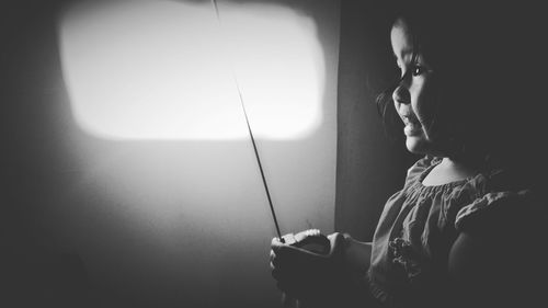 Side view of girl holding measuring tape on illuminated electric lamp