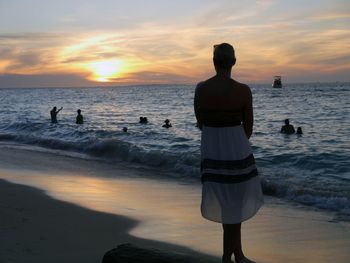 Rear view of men standing on beach against sky during sunset