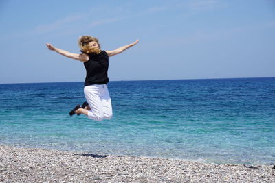 Full length of woman jumping at beach against sky