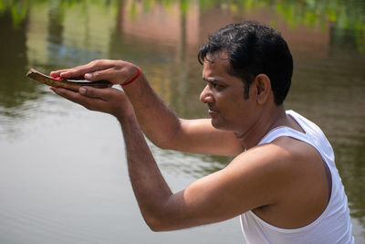 A young man is bowing to the sun on the bank of the river in the morning with a kosha in his hand 