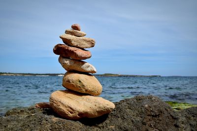 Stack of pebbles by sea against sky