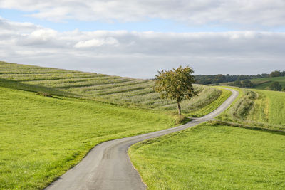 Scenic view of road amidst field against sky