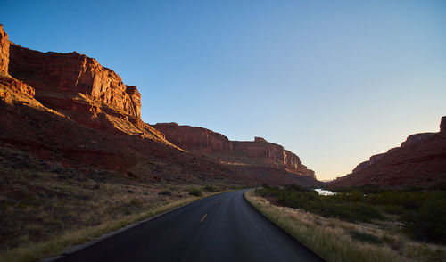 Road leading towards mountains against clear sky