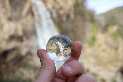 Close-up of hand holding crystal ball against sky