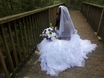 Bride sitting on footbridge in forest