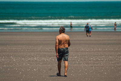 Rear view of shirtless man walking on beach