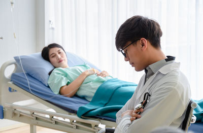 Doctor sitting with closed eyes while patient resting on bed in hospital
