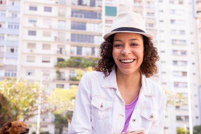 Portrait of smiling young woman standing against buildings 