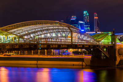 Illuminated sydney harbour bridge over river by buildings against sky at night