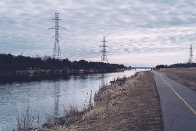 Empty road by river against cloudy sky