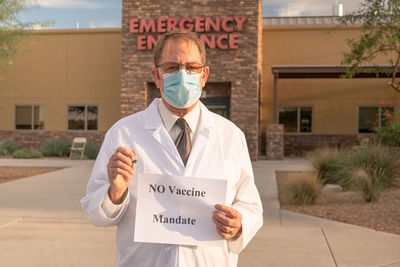 Portrait of doctor wearing mask holding paper with text