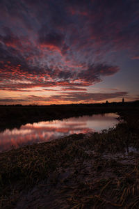 Scenic view of lake against dramatic sky during sunset