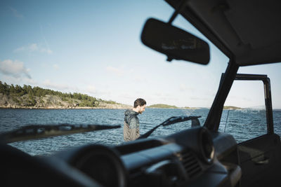 Man seen through car windshield at lakeshore