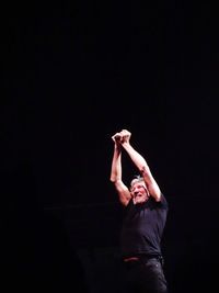 Man with arms raised standing against black background