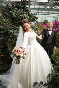 Bride holding bouquet walking with groom in garden