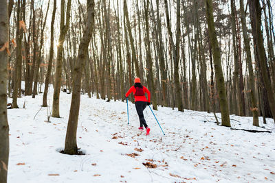 Back view of female trail runner jogging uphill with trekking poles on cold winter evening.