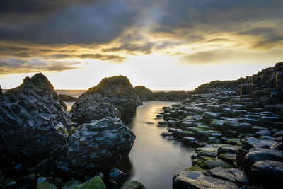 Rocks in sea against sky during sunset