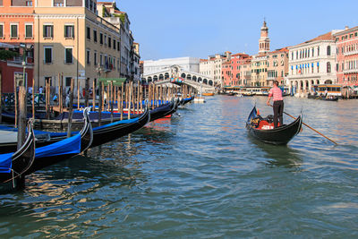 Rear view of man sailing gondola over grand canal against rialto bridge