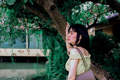 Woman looking away while standing by tree