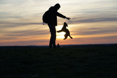 Silhouette men standing on field against sky during sunset