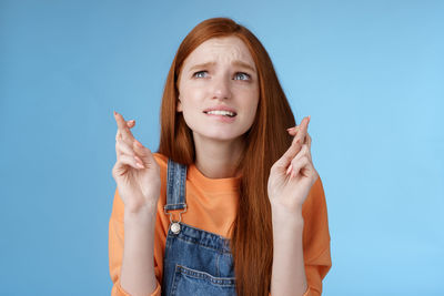 Worried woman with fingers crossed against blue background
