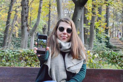 Portrait of woman showing mobile phone in forest