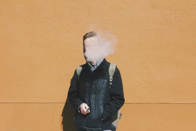 Man smoking while standing against yellow wall