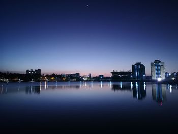 Sea by illuminated buildings against sky at dusk