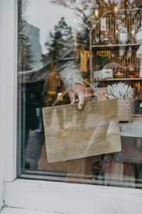 Male owner hanging open sign on store door seen through glass