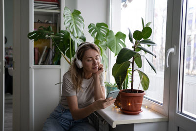 Young woman sitting on potted plant at home
