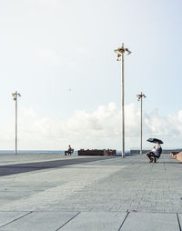 Man sitting on promenade at beach against sky