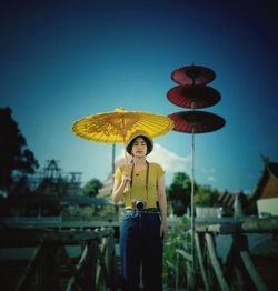 Portrait of woman with umbrella standing against blue sky