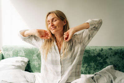 Young attractive blonde woman in sleepwear is stretching after waking up.