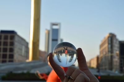 Close-up of hand holding crystal ball against clear sky