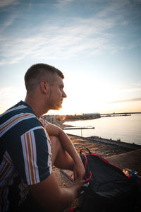 Pensive adult man in a striped t-shirt sitting on a bridge in helsinki, finland at sunset. 