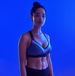 Portrait of young woman standing against blue background