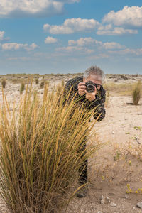 Gray haired adult male with glasses taking a photographs among the bushes.